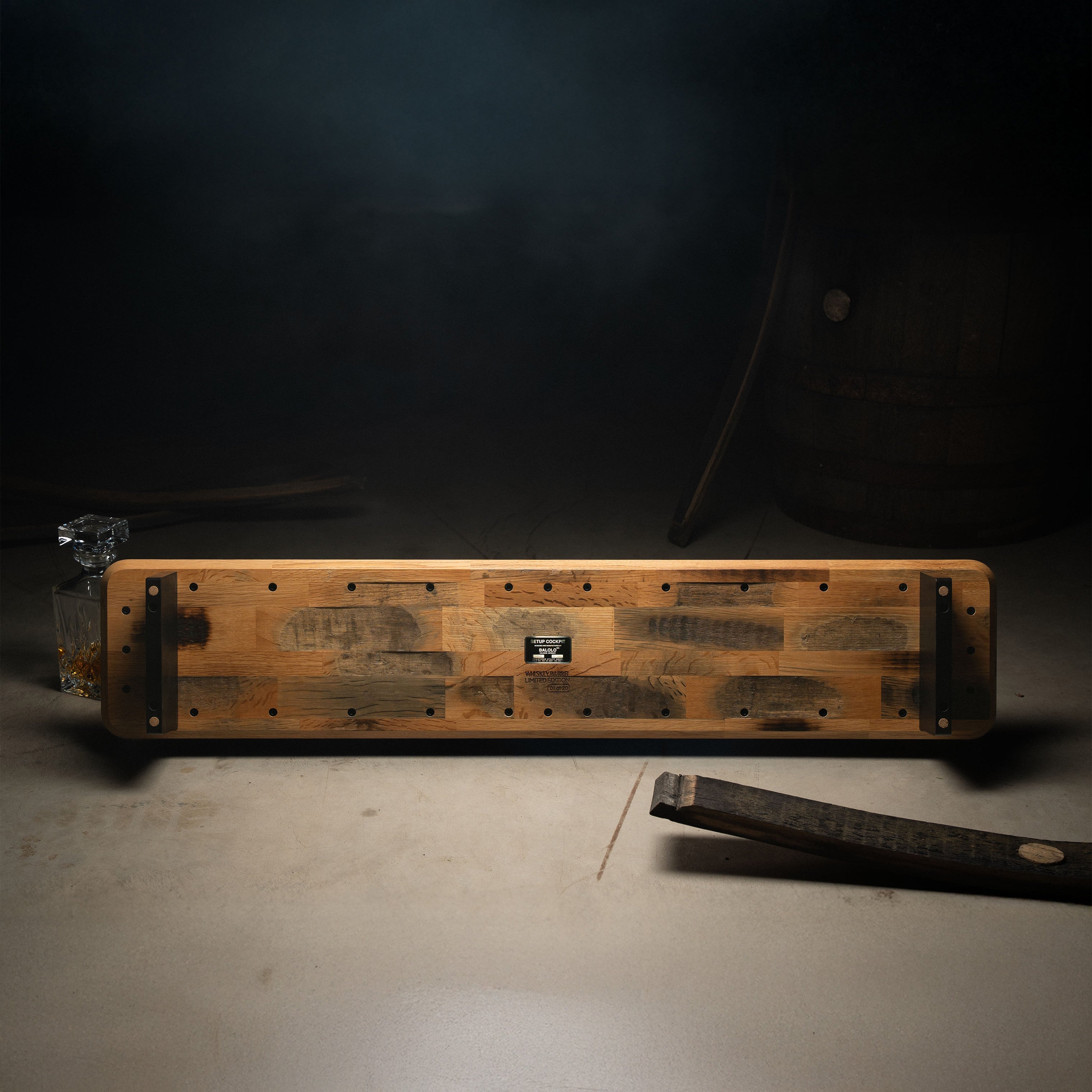 Hero Image der Whiskey Barrel Edition. Fokus auf Unterseite des Monitorständers, inszeniert in einer atmosphärischen Lagerhalle mit Fassdauben und Karaffe.