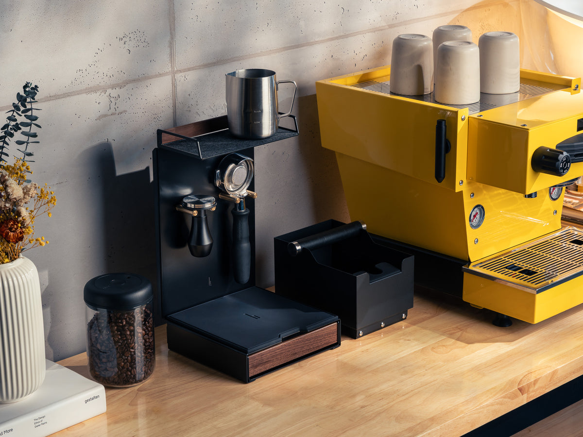 Barista Bar Nussbaum neben gelber Espressomaschine mit Tassen, Portafilter, Tamper und Kaffeebohnen-Glas auf einer Holzarbeitsplatte @expand #material_Amerikanischer Nussbaum