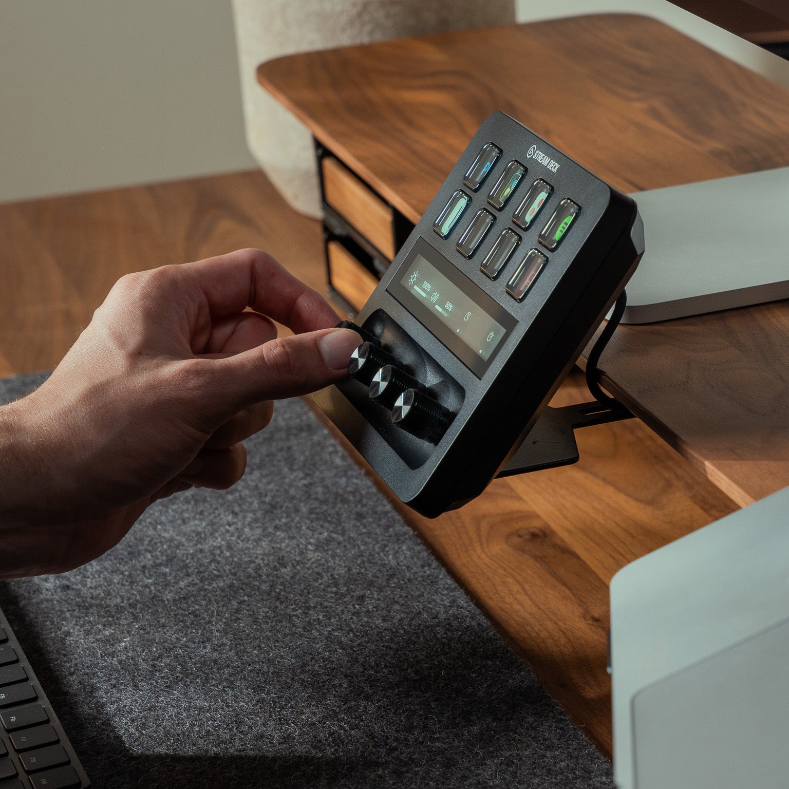 Detailaufnahme vom BALOLO Stream Deck Halter Plus am Setup Cockpit Monitorständer. Drehknopf des Elgato Stream Deck Plus wird von einer Hand bedient. In ästhetischem Office-Setup in Szene gesetzt.