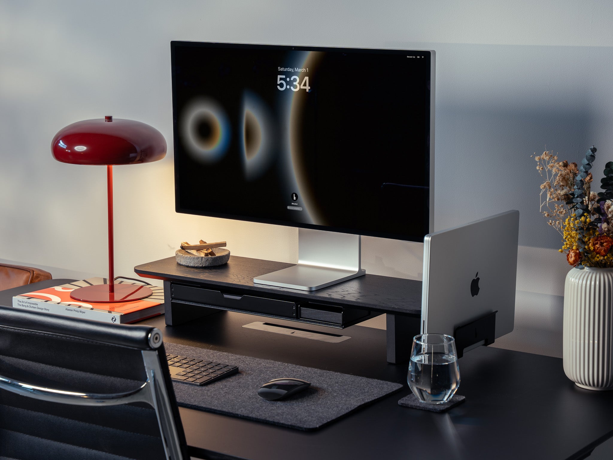 Setup Cockpit Medium aus schwarz gefärbter Eiche mit integrierten Anbauteilen: Laptop Dock, großes Fach, Stiftablage Large und Stiftablage, Kabelmagneten, Desk Pad und Desk Coaster. Abgebildet mit einem Apple Studio Display, Macbook, Tastatur und Maus in einem modernem Office Setting auf einem schwarzem Schreibtisch. @expand