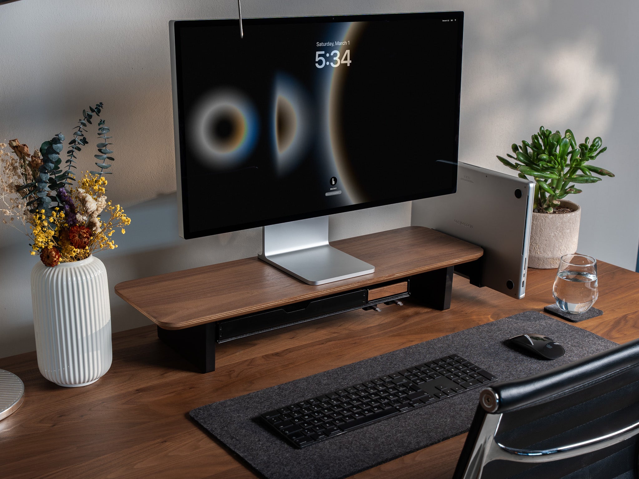 Setup Cockpit Monitorständer Medium aus Nussbaum mit Anbauteilen: Laptop Dock, großes Fach mit Stiftablage und Stiftablage Large, Kabelmagneten, Desk Pad und Desk Coaster. Abgebildet mit Apple Studio Display, Tastatur und Maus. Abgebildet auf Schreibtisch aus Nussbaum in modernem Home Office Setting. @expand