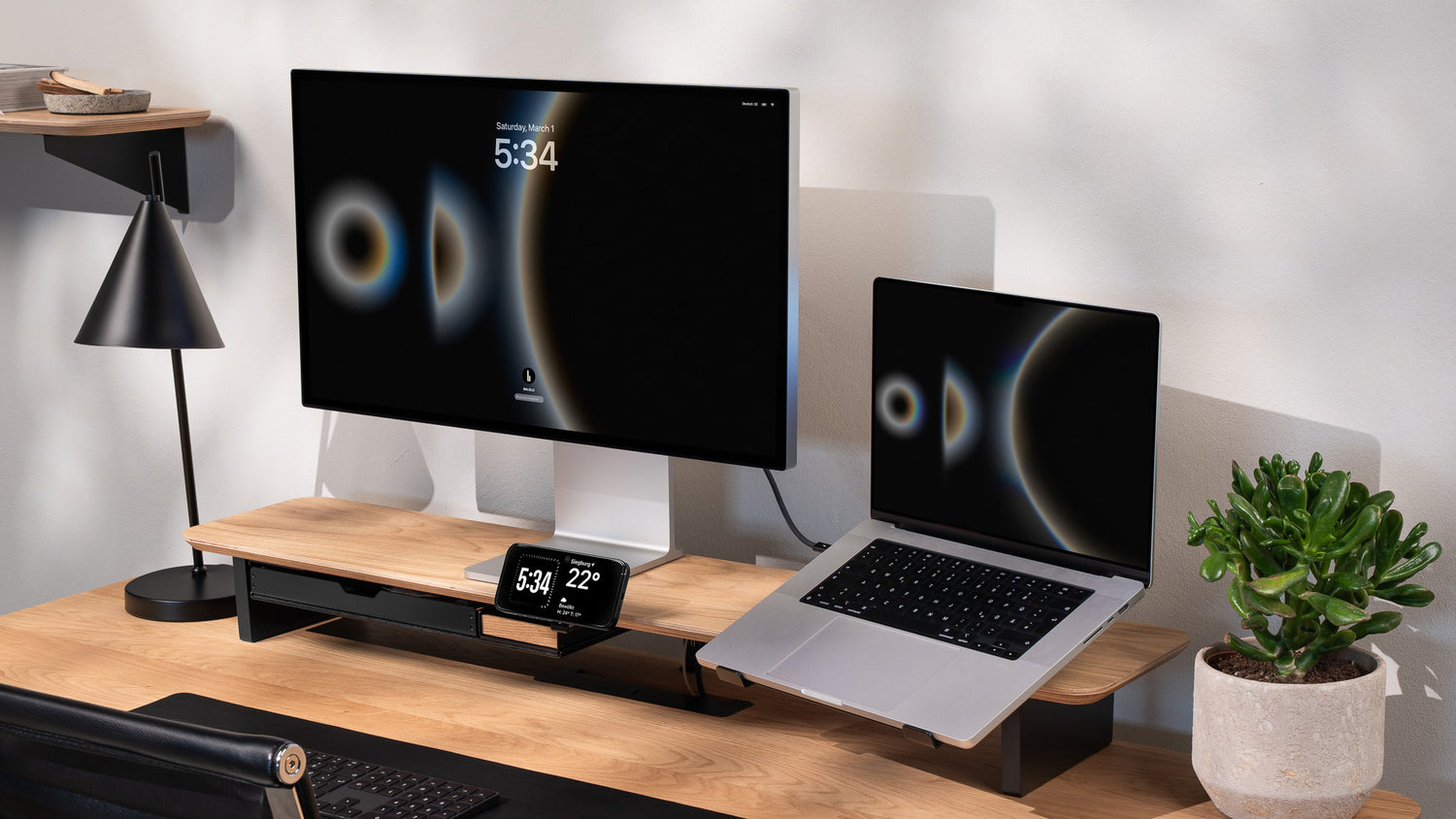 Totalaufnahme des BALOLO Setup Cockpit Monitorständer aus Eiche. Ausgestattet mit Laptophalter, MagSafe Halter, Ablagefach und Stiftablagen. Inszeniert in modernem Büro-Setting.