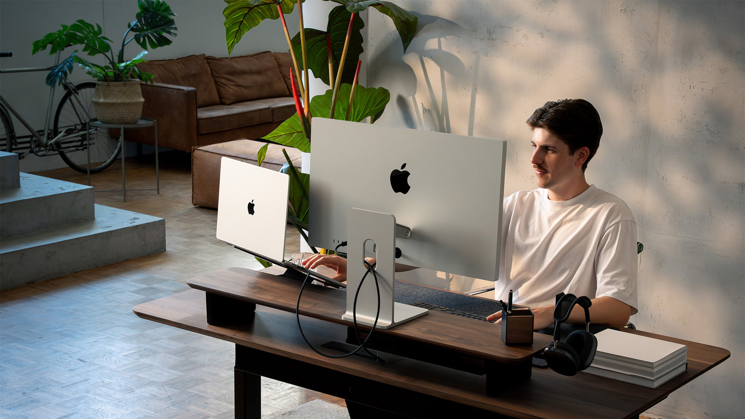 Person arbeitet am BALOLO Setup Cockpit Monitorständer aus Nussbaum mit Apple Studio Display